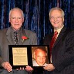 Two men holding a plaque and picture of a man.