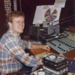 A man sitting at a mixing desk in front of a record player.