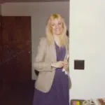 A woman in a purple dress and jacket standing next to a door.